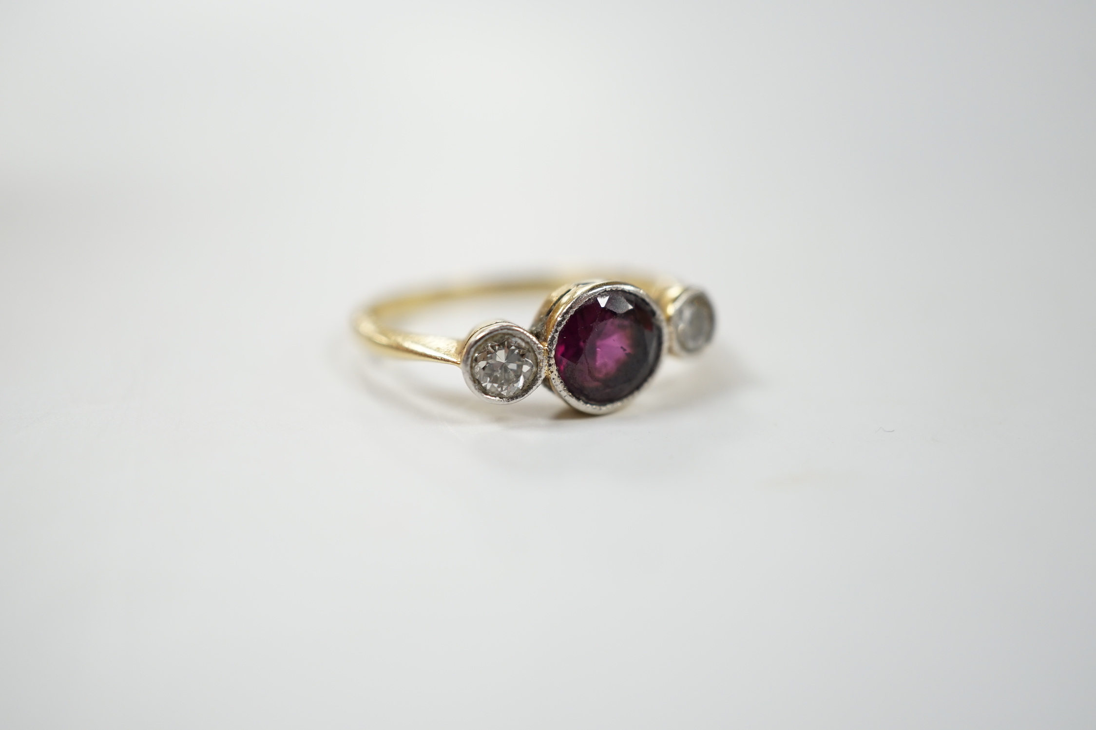 An early 20th century yellow metal and millegrain set single stone garnet and two stone diamond ring, size M, gross weight 2.8 grams.